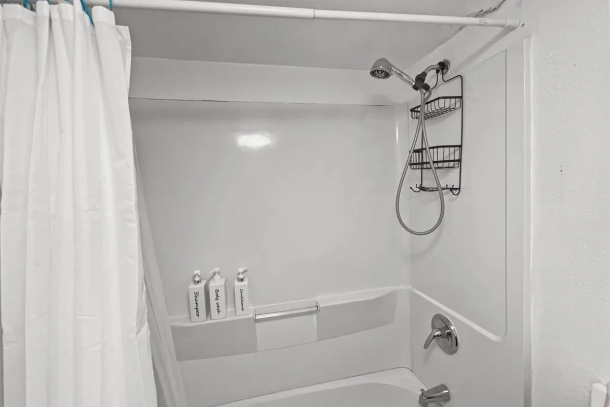 A clean, updated shower area with a modern showerhead, a stylish curtain, and a tidy shelf holding bath essentials. The space feels fresh and practical, suggesting a well-maintained environment designed for comfort and easy cleaning after sandy adventures.