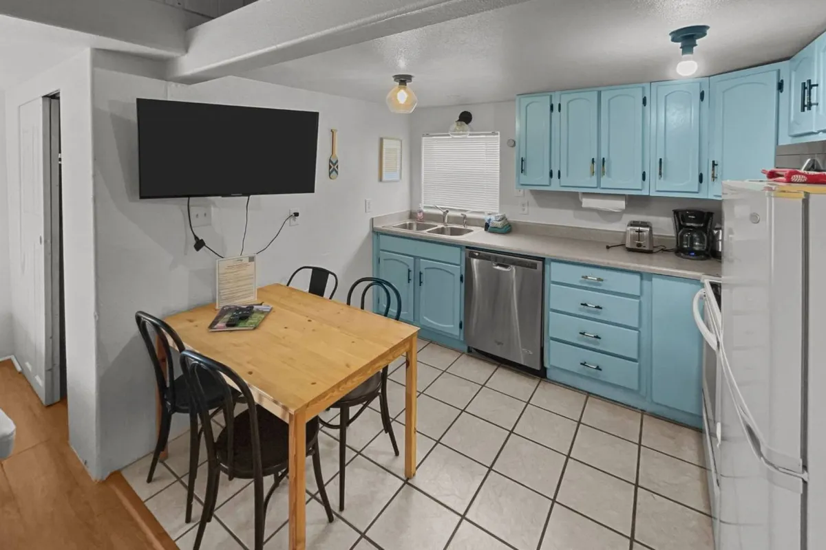 The focus of this image is the kitchen table surrounded by blue cabinets and appliances, suggesting a lively yet compact kitchen and dining area. The setup is friendly and inviting, with space for meals, games, or group activities, highlighting the multifunctionality of the space.