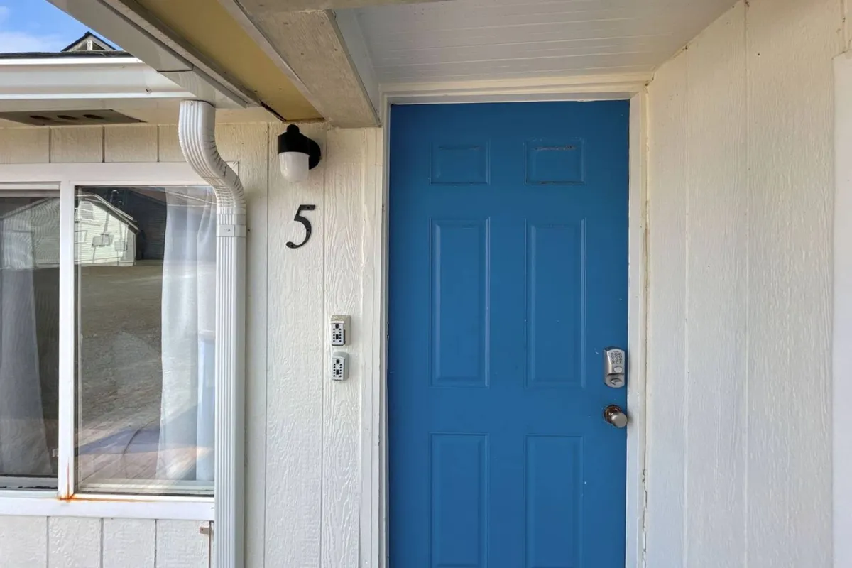 A front entry scene showing a welcoming blue door, clearly marked with the house number 5 and a bright light fixture above. The porch area is neat and inviting, hinting at easy access both into and out of the home, with space for guests and pets to pause or relax before heading inside or out for a walk.